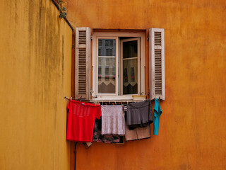 Clothes drying outside the window in the sunshine - Nice, Cote d'Azur, France. Colorful yellow house wall