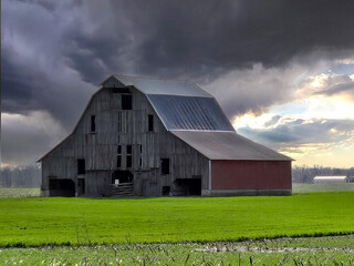 Vintage large wooden barn with storm clouds and green field - 784784239