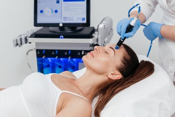 Middle aged beautician holding ultrasound device for hydro facial lifting and skin tightening...