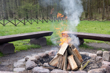 A fire in a resting place fenced with stones next to wooden benches