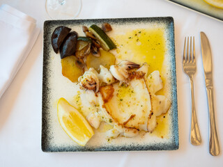 Popular dish of Spanish cuisine is grilled cuttlefish with garlic and parsley, served with calabasin potatoes and lemon