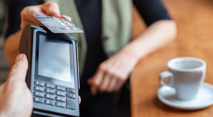 Young woman holding credit doing wireless bank payment with POS terminal process acquire at table in coffee shop cafe restaurant indoor. Focus on machine. Finance, restaurant industry, small business.