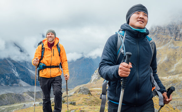 Caucasian and Sherpa men backpackers with trekking poles together hiking and enjoying Mera peak climbing acclimatization walk Makalu Barun Park route. Men enjoying Togetherness and beautiful valley.