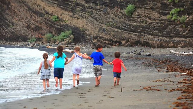 Children holding hands run along the seashore. Slow motion. High quality 4k footage