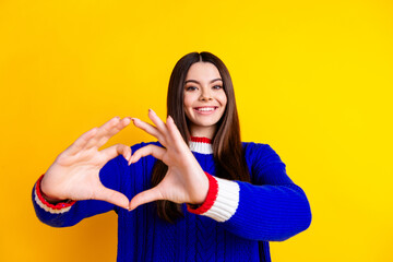 Photo portrait of pretty teen girl heart gesture hands wear trendy knitwear blue outfit isolated on yellow color background