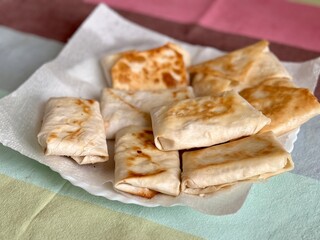 Fried pancakes-envelopes with cottage cheese, in form of envelopes in pita bread on white plate on table in background of a multicolored tablecloth