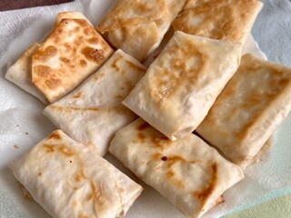 Fried pancakes-envelopes with cottage cheese, in form of envelopes in pita bread on white plate on table in background of a multicolored tablecloth