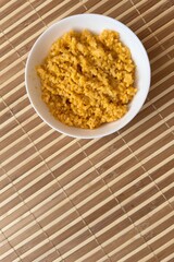 Yellow rice porridge cooked in milk with pumpkin spice in a white bowl on bamboo background. Close-up