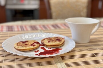 Healthy fritters with with lingonberry jam on a white ceramic plate next to white cup of coffee. Vegan breakfast food at the restaurant