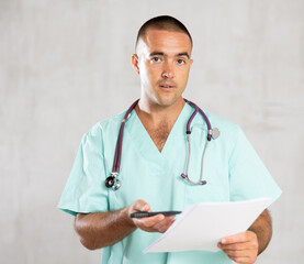 Portrait of male doctor in medical gown with stethoscope making notes in the patient medical history