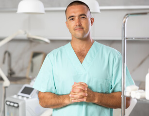 Portrait of positive male doctor cosmetologist wearing overall showing equipment of clinic before procedure