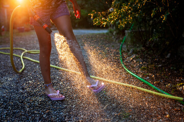 A playful moment captured as a child sprays water from a hose, the sunlight catching the mist...