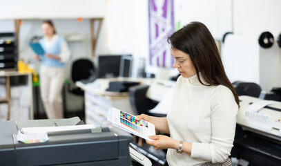 Printing office manager standing at printer and looking at colour test page for printer.