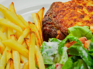 Burger with melted cheese toping, fresh green salad with lettuce and tomato and cucumber and fired potato chips on a wooden table. Tasty dinner. High quality product meal. Close up.