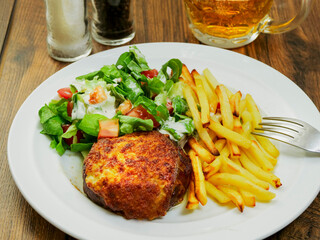 Burger with melted cheese toping, fresh green salad with lettuce and tomato and cucumber and fired potato chips on a wooden table. Tasty dinner. High quality product meal. Close up.