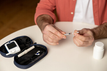 Unrecognizable diabetic man with insulin syringe injection sitting at table