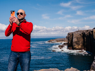 Tourist standing and enjoy view of stunning mini cliff in county Clare, Ireland. Travel and tourism. Bald man in red shirt, slim athletic body type in nature setting.