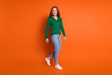 Fototapeta na wymiar Full length photo of excited funky lady dressed green shirt walking empty space isolated orange color background