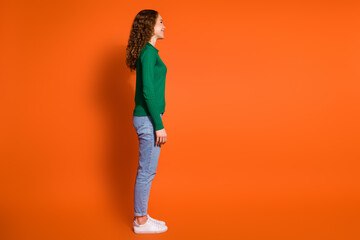 Full length photo of slim cheerful lady dressed green shirt looking emtpy space isolated orange color background