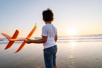 Child with plane, poised for play at sunset shore.