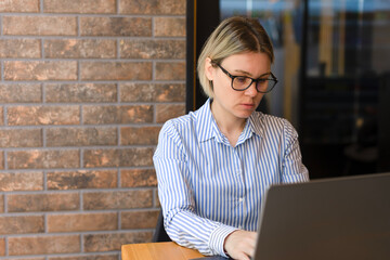 A woman with glasses is doing business in the office on a laptop. Young woman working, freelancer, telecommuting, not at home, business woman. A girl student studies on a laptop, performs tasks