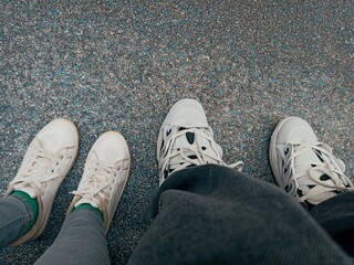 Selfie of man and woman legs in white sneakers standing on the floor