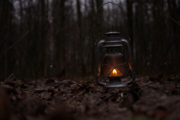 Fototapeta premium Old kerosene lamp shines in the brown autumn leaves