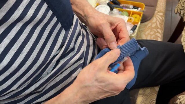 Unknown adult man sitting on the couch repairing and cuts clothes with a special blade and separates pieces of fabric from each other. Close-up