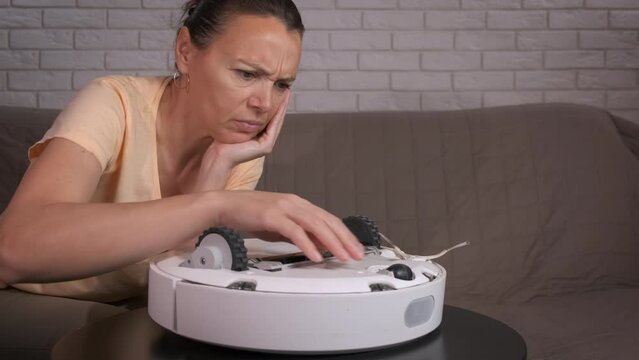 Broken robot cleaner on table. An uphappy woman have household trouble with broken vacuum cleaner indoor.