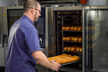 Man baker holding baguettes on oven