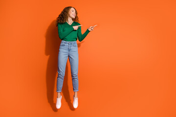 Fototapeta na wymiar Full length photo of cute dreamy lady dressed green shirt jumping high showing two fingers emtpy space isolated orange color background