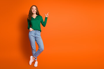 Full length photo of dreamy sweet lady dressed green shirt pointing empty space isolated orange color background
