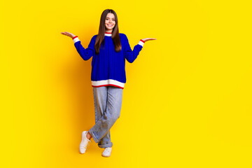 Full length photo of pretty teen girl compare empty space wear trendy knitwear blue outfit isolated on yellow color background