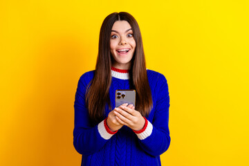 Photo portrait of pretty teen girl hold gadget excited wear trendy knitwear blue outfit isolated on yellow color background