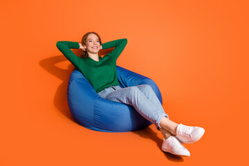 Full length photo of cute dreamy lady dressed green shirt relaxing bean bag arms behind head isolated orange color background