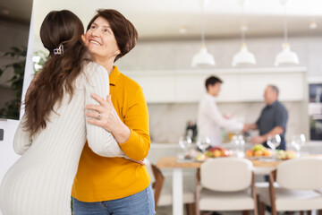 Positive young girl warmly welcoming with hug and kiss senior woman, coming family celebration at...