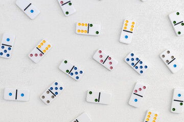 White dominoes with colorful dots on a white cement background, top view. Board game. - obrazy, fototapety, plakaty