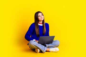 Full length photo of pretty teen girl hold netbook look empty space wear trendy knitwear blue outfit isolated on yellow color background