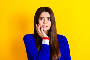 Photo portrait of pretty teen girl nervous bite nails wear trendy knitwear blue outfit isolated on yellow color background