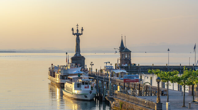 Blick auf die Hafeneinfahrt mit Imperia-Statue, dem Bodensee mit Katamaran F&auml;hre und Landschaftspanorama bei Sonnenaufgang. Konstanz, Bodensee, Baden-W&uuml;rttemberg, Deutschland, Europa.