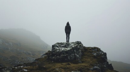 A person stands on a rocky outcrop back facing the camera as they bravely face the misty mountain pass leading to the rumored . . - obrazy, fototapety, plakaty