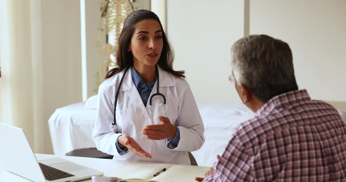 Confident Hispanic doctor woman giving consultation to elderly Indian patient, explaining medical recommendation for treatment, talking to senior man after examination, discussing diagnosis