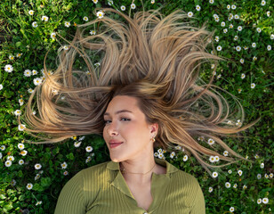 Top view Pretty blonde girl with healthy hair laying on grass with daisies , looking at camera