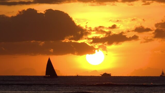 HAWAII - 3.19.2024 - Sailboats and a yacht move off the coast of Hawaii at sunset.
