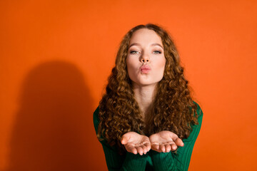 Photo of dreamy flirty lady dressed green shirt sending you kiss arm emtpy space isolated orange color background