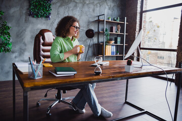 Fototapeta na wymiar Photo of cheerful lovely relaxed woman enjoying morning tasty coffee looking monitor modern office workspace workstation