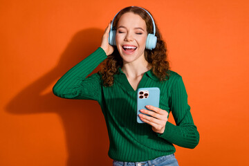 Photo of excited good mood lady dressed green shirt headphones enjoying music modern gadget isolated orange color background