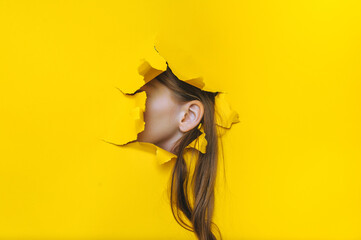 Left female ear and long hair close-up. Copy space. Torn paper, yellow background. The concept of eavesdropping, espionage, gossip and the yellow press.