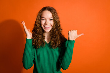 Photo of cheerful impressed lady dressed green shirt showing thumb emtpy space isolated orange color background
