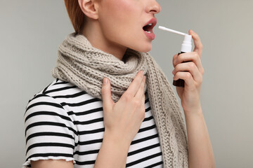 Young woman with scarf using throat spray on grey background, closeup